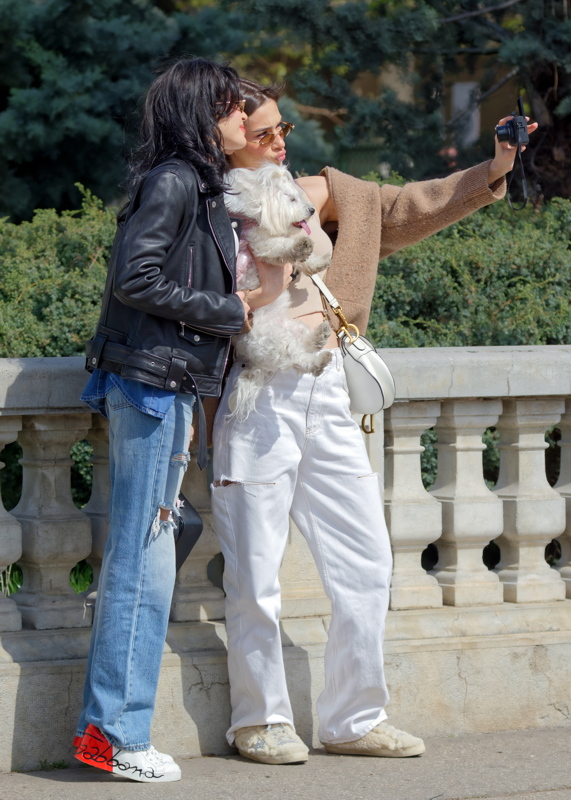 Two girls with a little dog posing on sidewalk